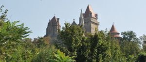 Ein Schloss steht auf einem Hügel, umgeben von dichter Vegetation. Das Schloss hat mehrere Türme, jeder mit einem einzigartigen Design.