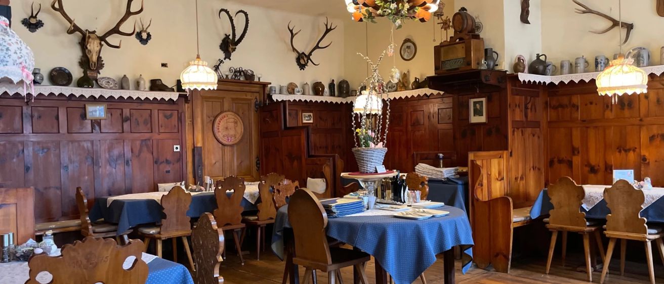 Ein gemütliches Esszimmer mit hölzernen Wänden, Böden und Möbeln. Es gibt Geweihe und Vintage-Artikel an den Wänden. Ein Tisch mit blauer Tischdecke und einer Vase mit Blumen ist gedeckt.