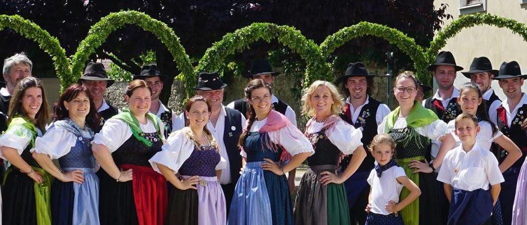 Eine Gruppe von Menschen in traditioneller bayerischer Kleidung posiert für ein Foto vor einem Gebäude.