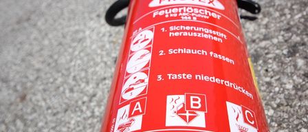 Ein roter Protex-Feuerlöscher mit Anweisungen auf Deutsch. Er ist für elektrische Brände und Spannungen über 1000 Volt. Er wiegt 6 kg.