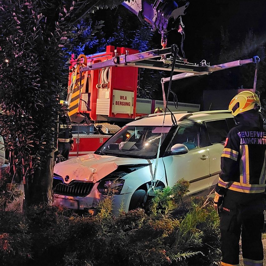 Ein Feuerwehrauto steht neben einem beschädigten Auto. Eine Person mit gelbem Helm steht neben dem Fahrzeug.