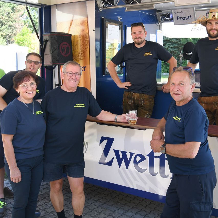 Eine Gruppe von Menschen in blauen T-Shirts posiert vor einem Food Truck. Ein Mann hält ein Glas Bier.