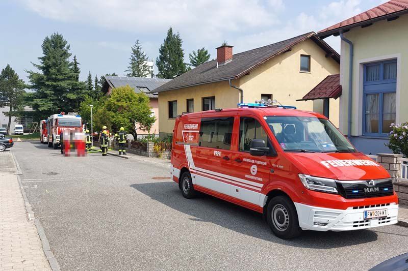 Ein roter Feuerwehrwagen und ein weißer Van sind auf der Straße geparkt. Feuerwehrleute sind in der Nähe und bereiten sich auf einen Vorfall vor.