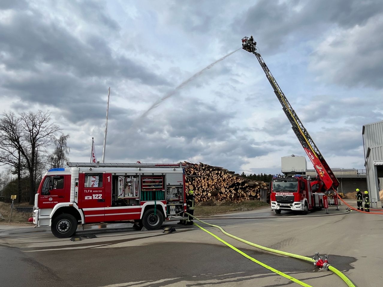 A fire truck with the number 122 sprays water from a ladder onto a pile of wood on a cloudy day.