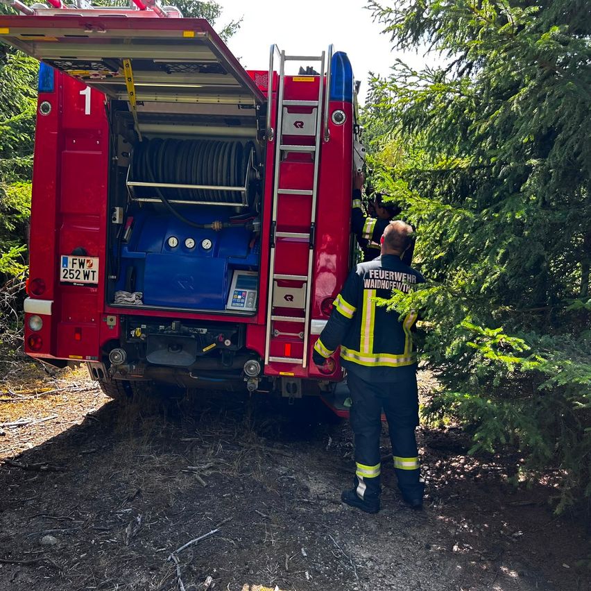 Ein Feuerwehrmann steht neben einem roten Feuerwehrauto mit der Nummer 1 auf der Rückseite, die Rückseite des Autos ist geöffnet und eine Leiter ist ausgefahren.