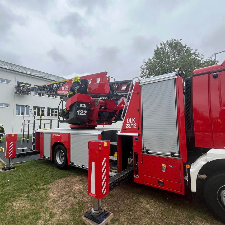 A red fire truck with a ladder extended is parked in front of a building. A firefighter is on the ladder.