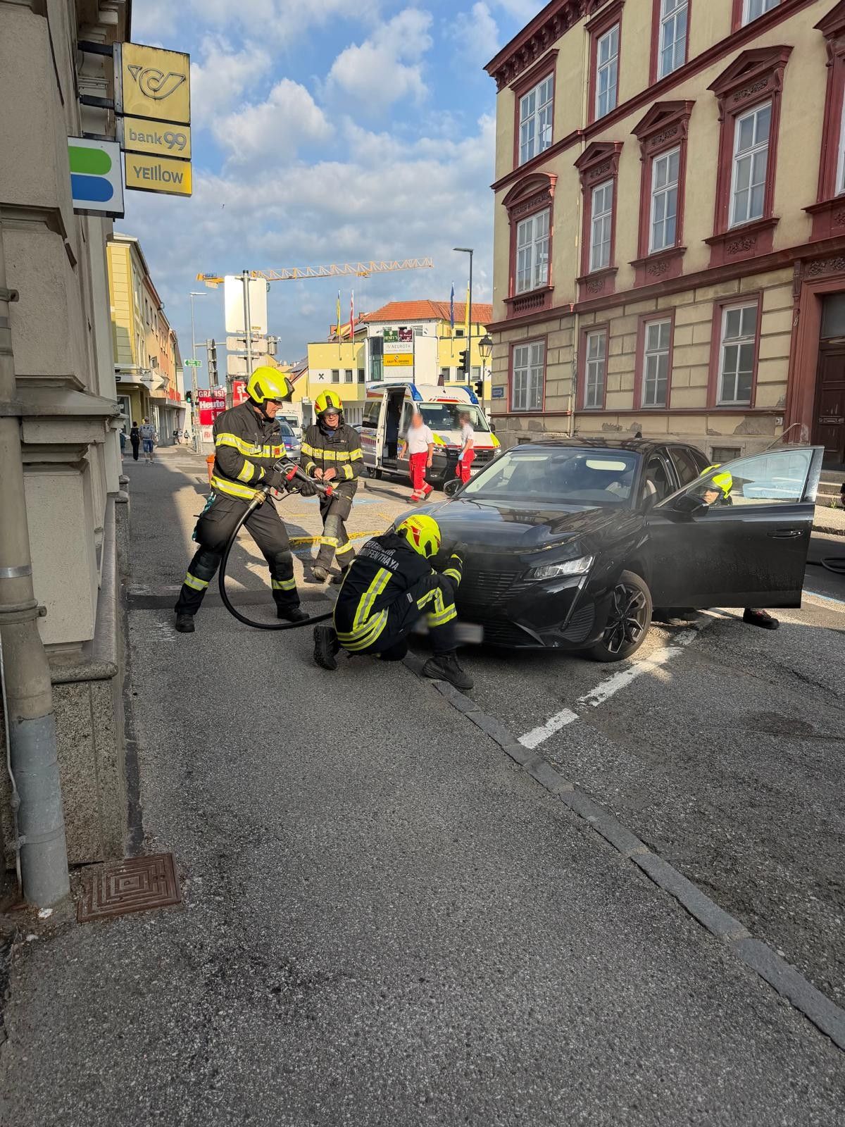 Drei Feuerwehrleute kümmern sich um einen Autounfall. Sie tragen gelbe Helme und Uniformen und arbeiten daran, jemanden aus dem beschädigten Auto zu befreien.