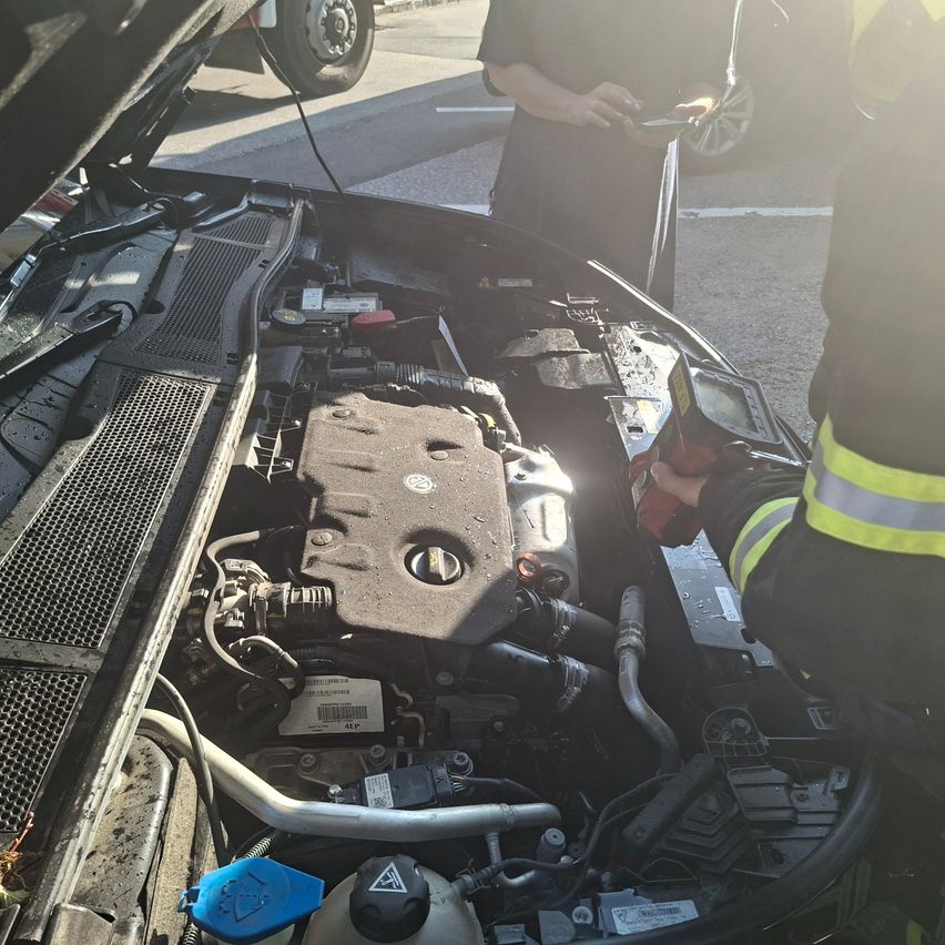 Der Motor eines Autos ist geöffnet und wird von zwei Personen überprüft. Eine Person hält ein Gerät, möglicherweise ein Diagnosewerkzeug.