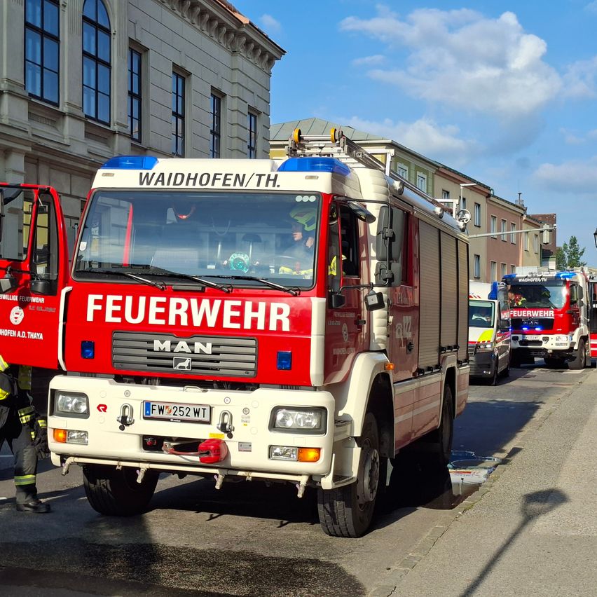 Ein roter und weißer MAN Feuerwehrwagen steht auf der Straßenseite, mit anderen Fahrzeugen dahinter.