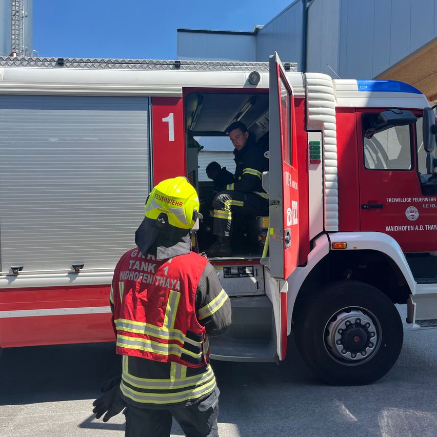 Zwei Feuerwehrleute bereiten einen Feuerwehrwagen vor, einer sitzt im Inneren und der andere steht draußen in einem gelben Helm.