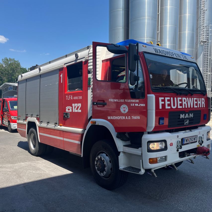 Ein roter Feuerwehrwagen mit der Nummer 1 an der Seite ist neben anderen Fahrzeugen vor großen Silos geparkt.