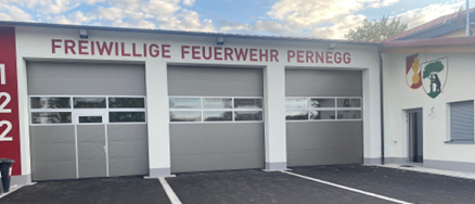 Die Vorderseite eines Gebäudes mit drei Garagen, beschriftet mit Freiwillige Feuerwehr Pernegg, Nummern 1, 2 und 3. Das Gebäude hat ein Schild und Fenster auf der rechten Seite.