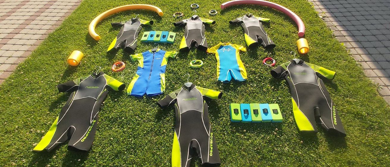 Verschiedene Neoprenanzüge, Schnorchel und Zubehör auf Gras ausgelegt, möglicherweise für eine Tauchveranstaltung.