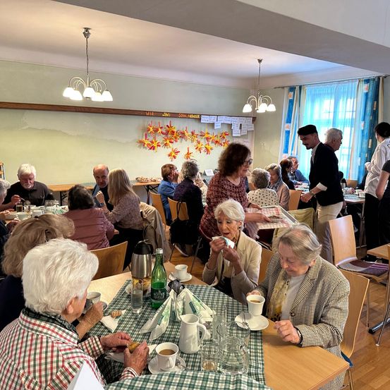 Eine Gruppe älterer Menschen speist gemeinsam in einem Restaurant mit Herbstdekoration an der Wand, und ein Kellner bedient sie.