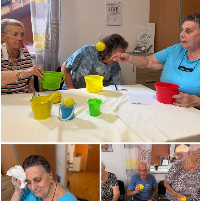 A group of elderly individuals are engaged in a game involving buckets and tennis balls, with one person holding a ball and another reaching for a bucket.