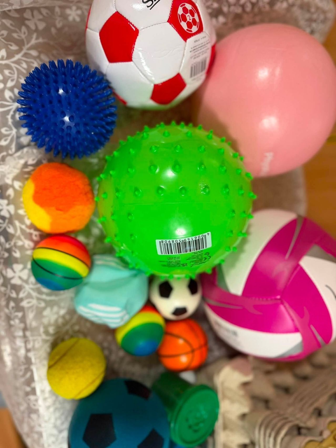 Eine Sammlung von bunten und strukturierten Bällen, einschließlich eines grünen spitzen Balls, eines blauen spitzen Balls und eines rosa Luftballons, auf einer gemusterten Oberfläche angeordnet.