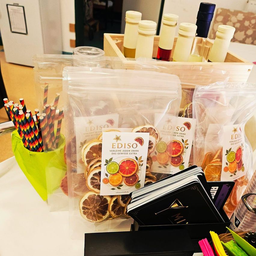 Ein Tisch zeigt eine Vielzahl von zitrusaromatischen Produkten, einschließlich getrockneter Zitrusscheiben, einer Box mit Weinflaschen und einer Box mit EDISO-Produkten.