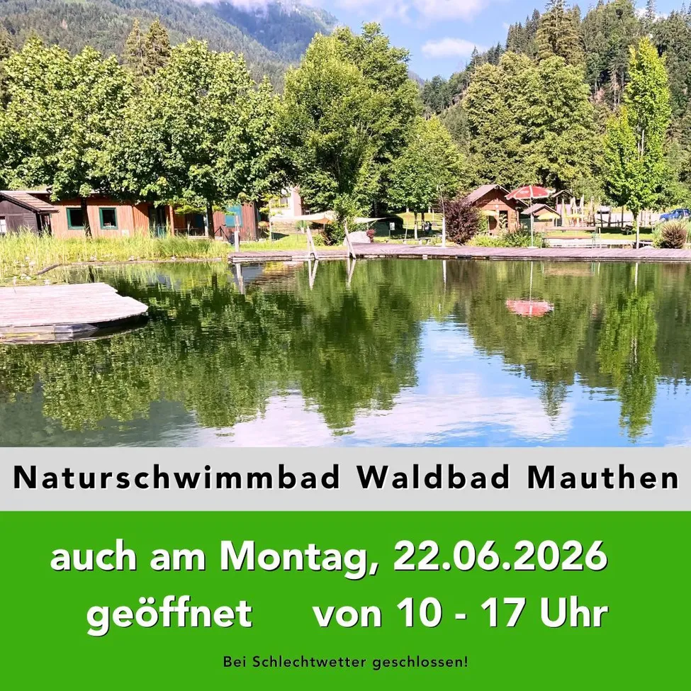 Ein ruhiger See mit einem hölzernen Steg umgeben von Bäumen und Häusern. Ein Schild zeigt Naturschwimmbad Waldbad Mauthen, geöffnet bis 17 Uhr am Montag, 22.06.2026.