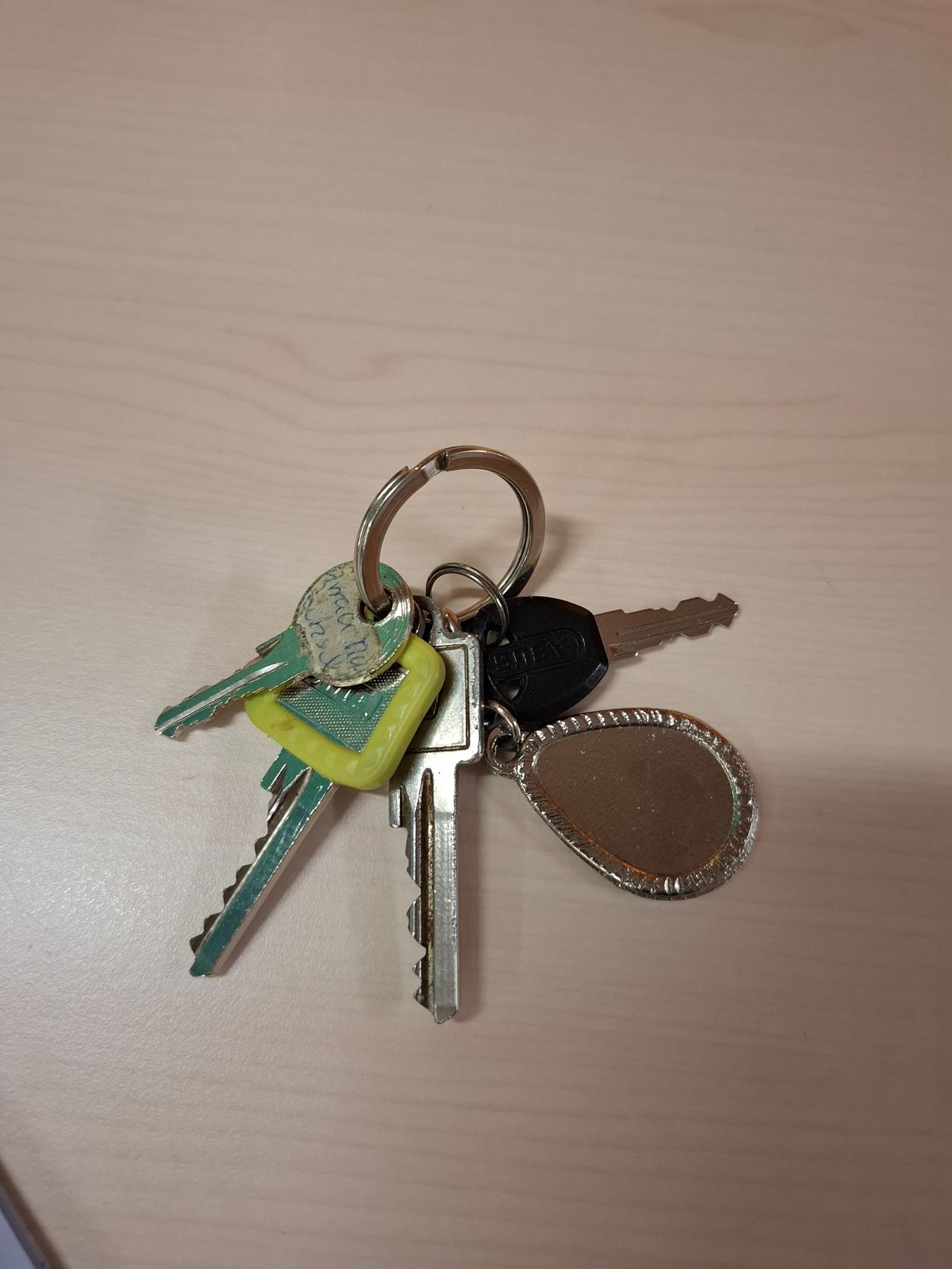 Mehrere Schlüssel mit verschiedenen Schlüsselanhängern liegen auf einer hellen Holzoberfläche. Ein Schlüssel hat einen gelben Griff.