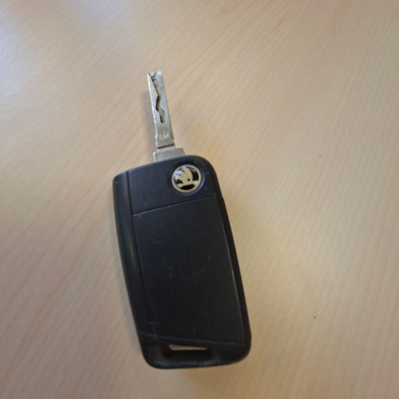 Ein schwarzer Autoschlüssel mit einer silbernen Klinge und einem Logo am Kopf, auf einer Holzoberfläche platziert.