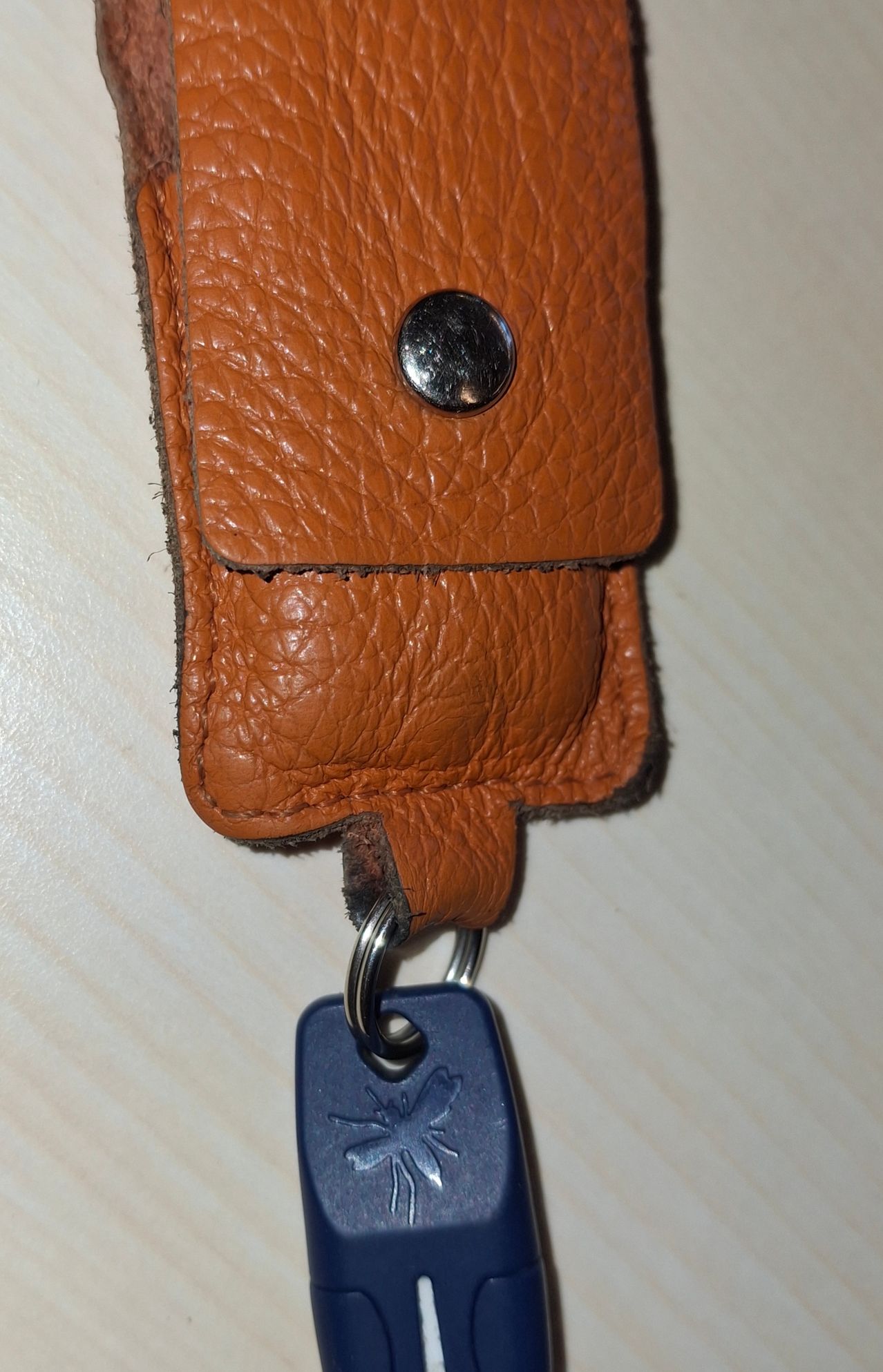 Ein brauner Lederschlüsselanhänger mit einem blauen Anhänger mit Vogellogo. Der Schlüsselanhänger sieht abgenutzt aus und hat einen kleinen schwarzen Knopf.