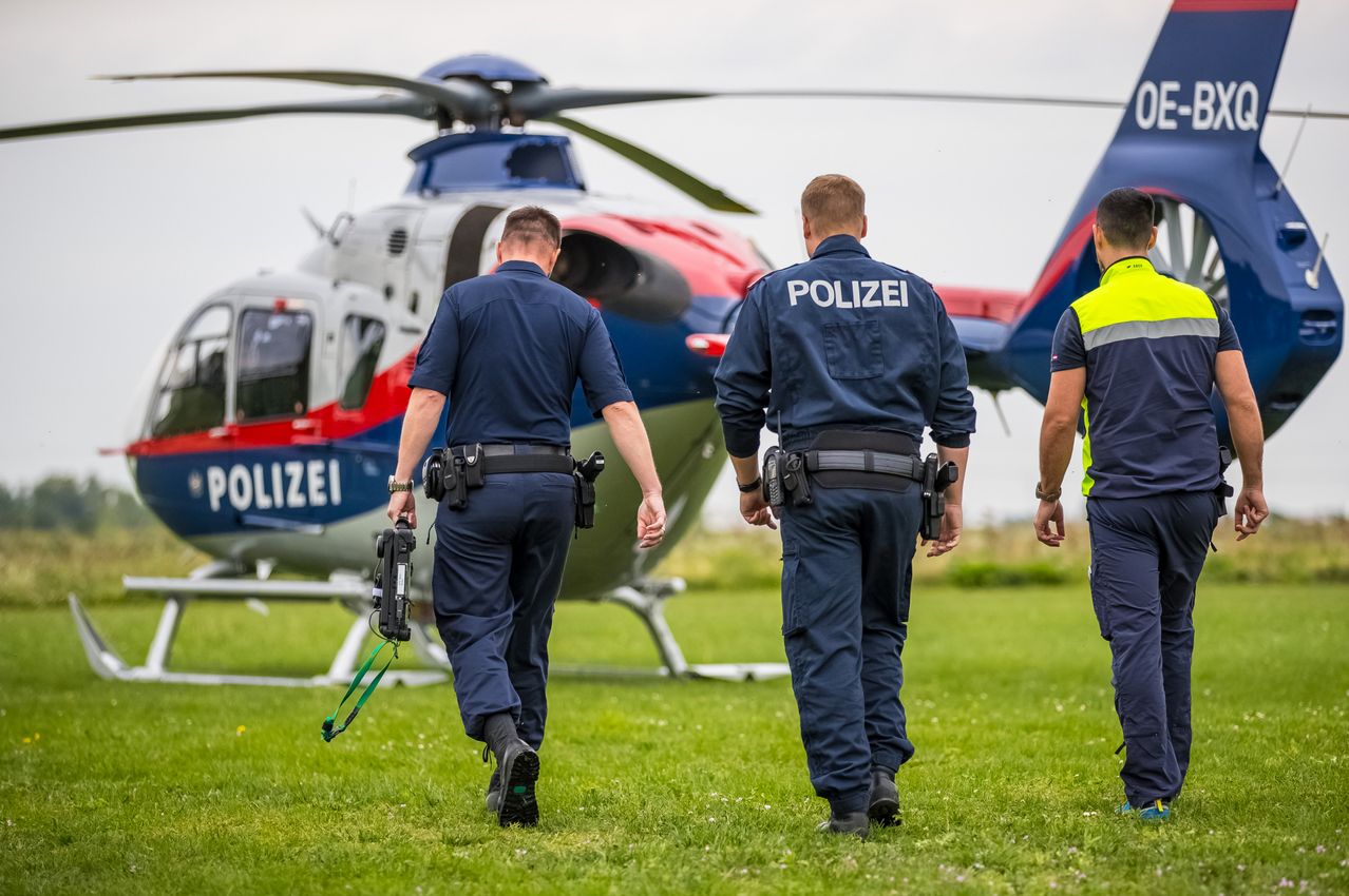 Drei Polizeibeamte laufen auf Gras in der Nähe eines Polizeihubschraubers. Sie tragen Marineuniformen und tragen Ausrüstung.