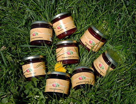 Sieben Gläser Marmelade liegen auf dem Rasen, eines davon offen und eine Distel in der Mitte.