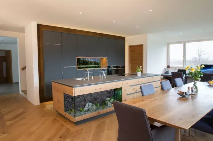 An open concept kitchen with wooden floors, a large island, aquarium, and a dining table with flowers and bowls.