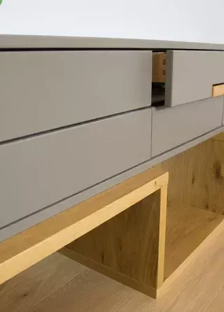 Ein moderner, hölzerner Medienschrank mit vier Schubladen und einer offenen Schublade, auf einem hölzernen Boden. Der Schrank ist grau mit hölzernen Akzenten.