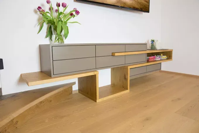 Ein modernes Holz-Entertainment-Center mit Schubladen und einer Vase mit Tulpen darauf, in einem Raum mit weißer Wand.