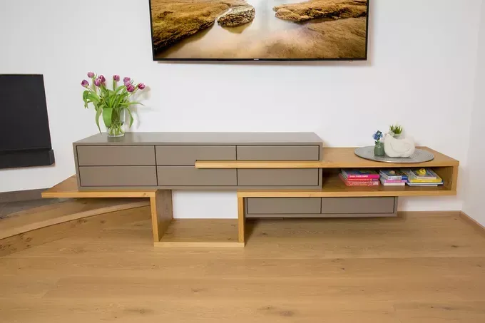 Ein modernes TV-Gestell mit Blumenarrangement, einer Schale, Büchern und einem Fernseher, der an der Wand darüber montiert ist.