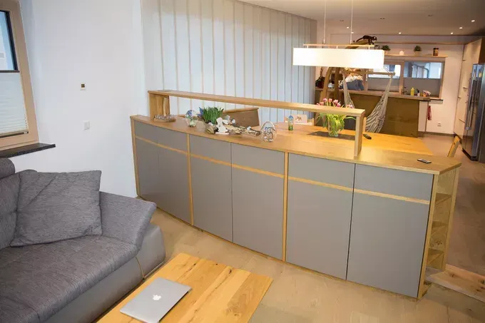 Ein modernes Wohnzimmer mit einer Couch, einem holzfarbenen Couchtisch und einer Kücheninsel mit Pflanzen und einer Lampe.
