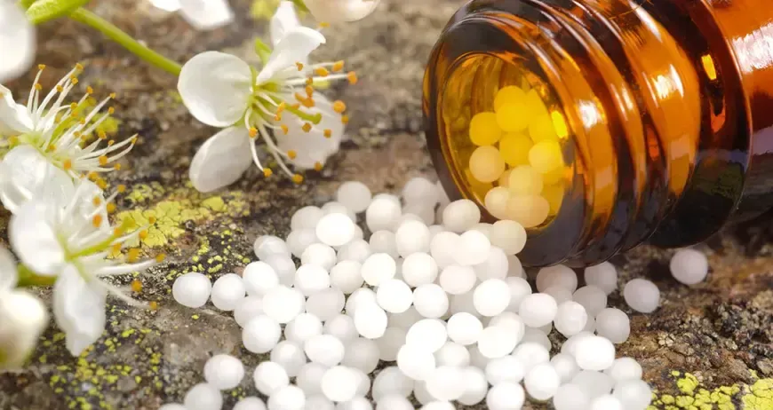 Eine braune Glasflasche mit einigen gelben und weißen Pillen ist geöffnet und verschüttet ihren Inhalt auf einer rauen Oberfläche. Im Hintergrund befinden sich weiße Blumen mit gelben Zentren.