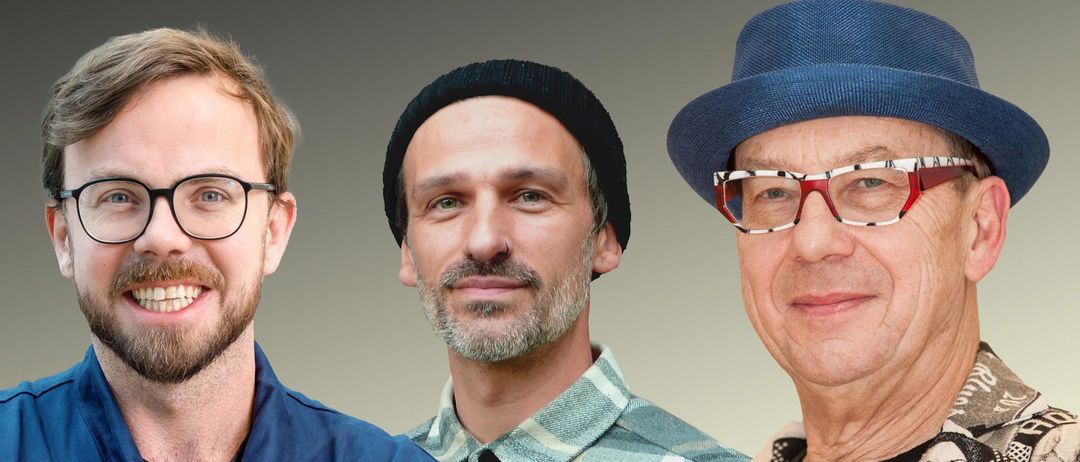 Zwei bärtige Männer, einer in einem karierten Hemd und einer Mütze, der andere in einem blauen Hut und mit Brille. Sie lächeln beide.