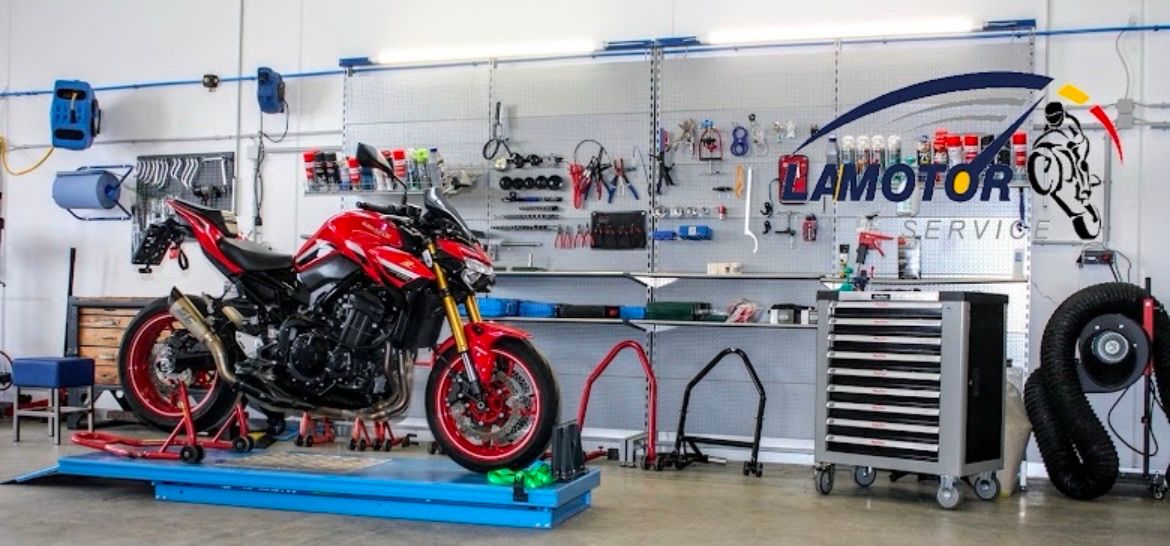 A red motorcycle is on a lift in a well-organized garage with various tools and equipment on the walls and shelves.