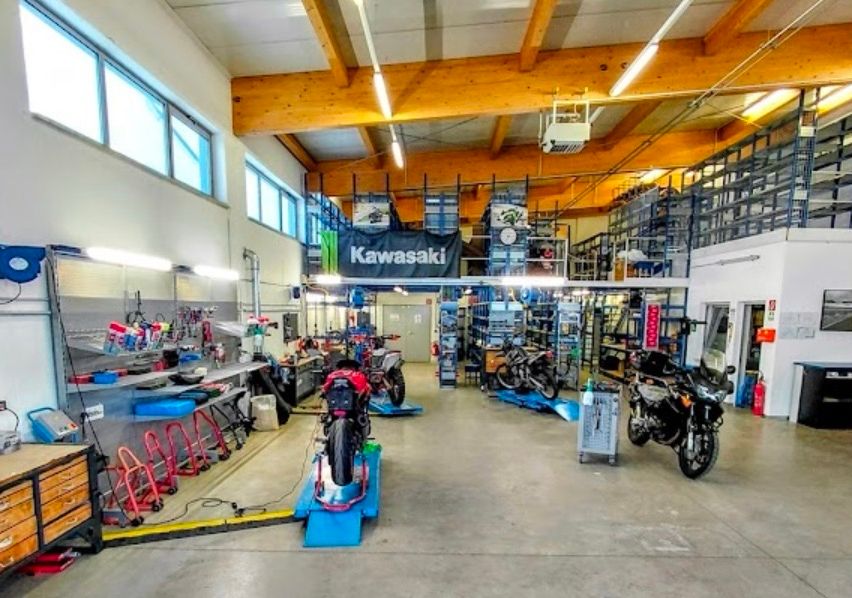 A motorcycle repair shop with several motorcycles on display and tools on the shelves. The shop has wooden beams and a Kawasaki banner.