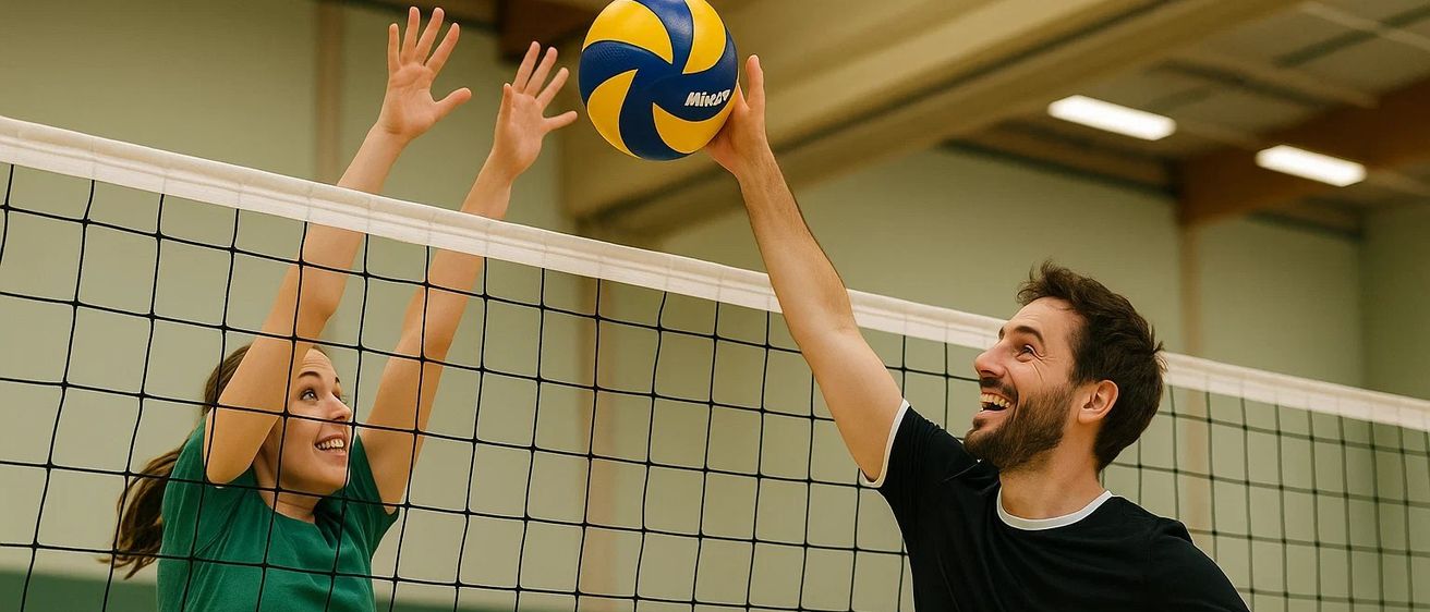 Ein Mann und eine Frau spielen Volleyball in einer Turnhalle, wobei die Frau nach oben schlägt, um den Ball zu treffen.