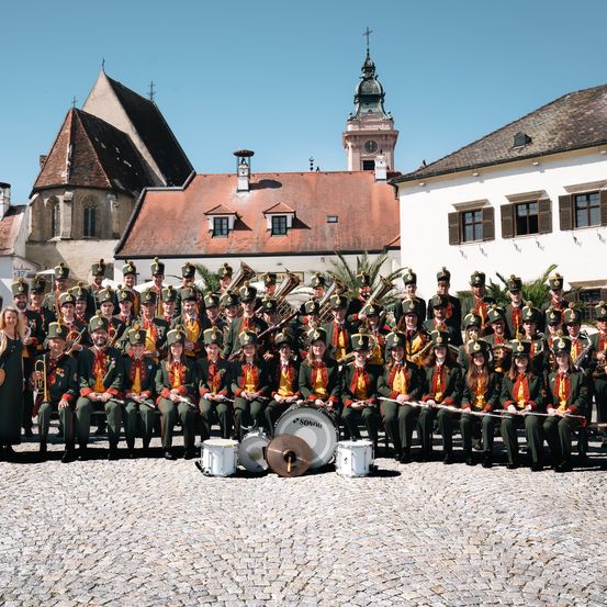 Ein großes Marschorchester in grünen und gelben Uniformen posiert für ein Foto vor einem historischen Gebäude.