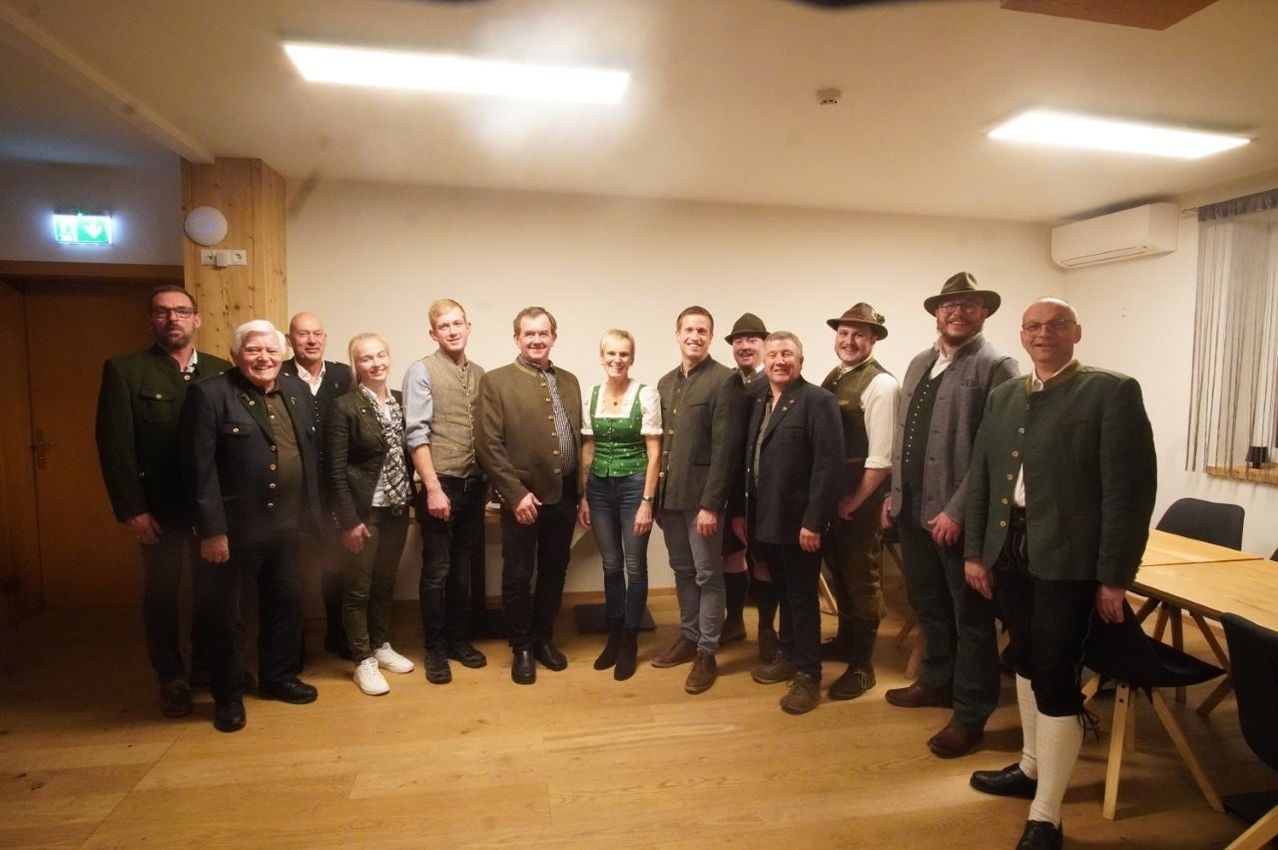 Eine Gruppe von Menschen in traditioneller Kleidung posiert für ein Foto in einem Raum mit Holzboden und weißen Wänden.