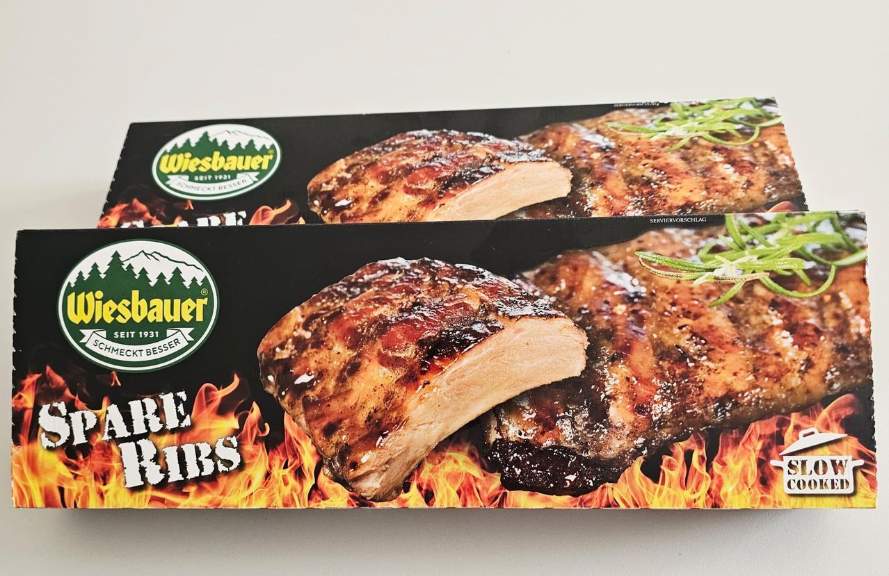 Pakete von Wiesbauer BBQ-Rippchen mit flammenartigem Design auf weißem Hintergrund. Das Fleisch hat eine knusprige Glasur.