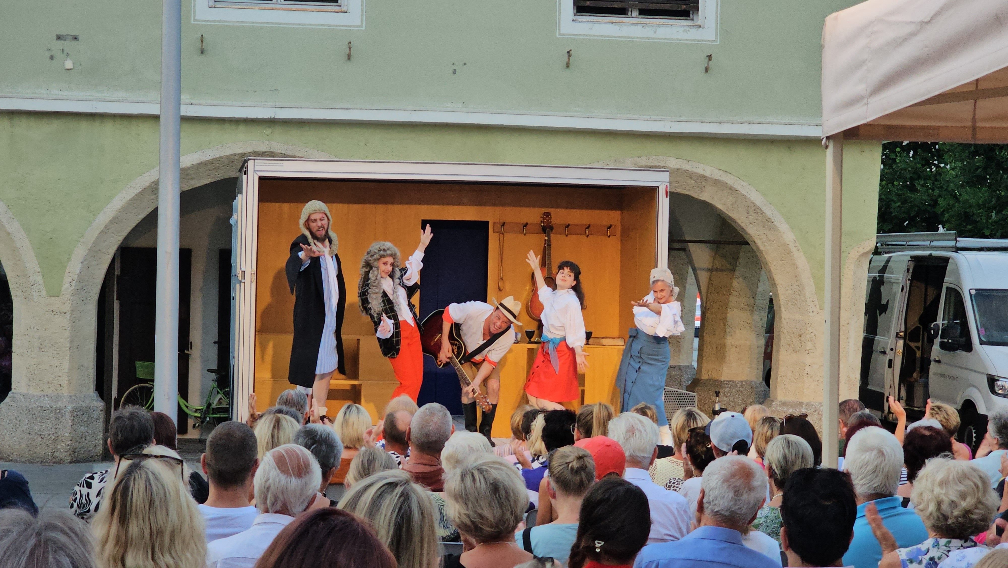Vier Personen spielen auf einer Bühne mit Gitarren vor einem Publikum in einem Raum mit gewölbten Durchgängen.