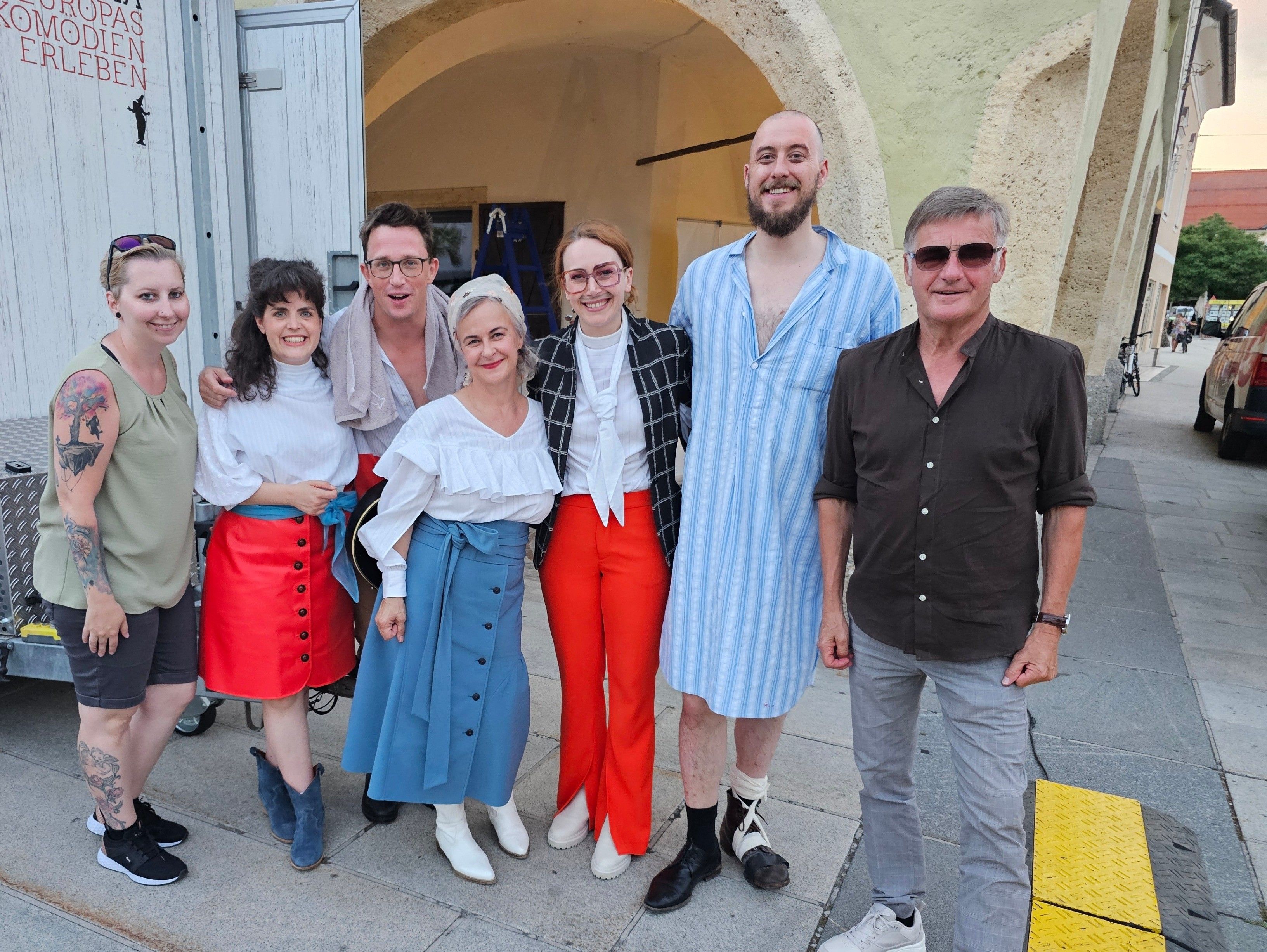 Eine Gruppe von Menschen, einige mit Brille, posiert für ein Foto auf einem Bürgersteig vor einem Bogen.