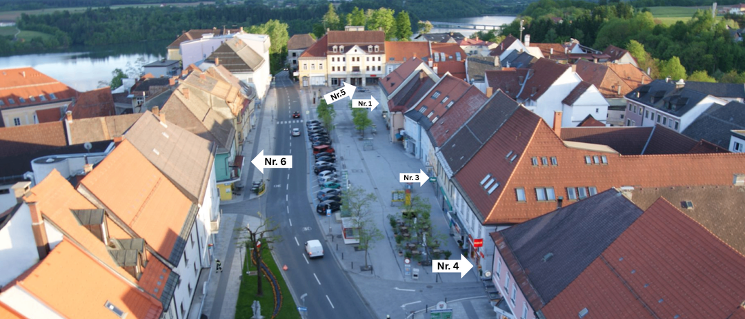 Luftaufnahme einer Stadt mit mehreren Gebäuden und geparkten Autos. Die Straße hat die Nummern 1 bis 6, und mehrere Personen arbeiten an der Seite. Bäume und Gras sind vorhanden.