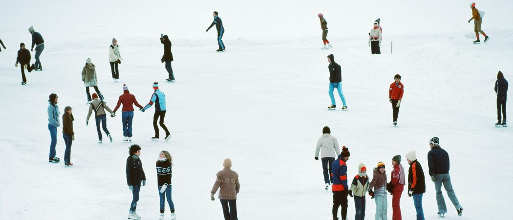 Eine Gruppe von Menschen schlittert auf einem zugefrorenen See. Sie tragen Winterkleidung und einige halten sich an den Händen.