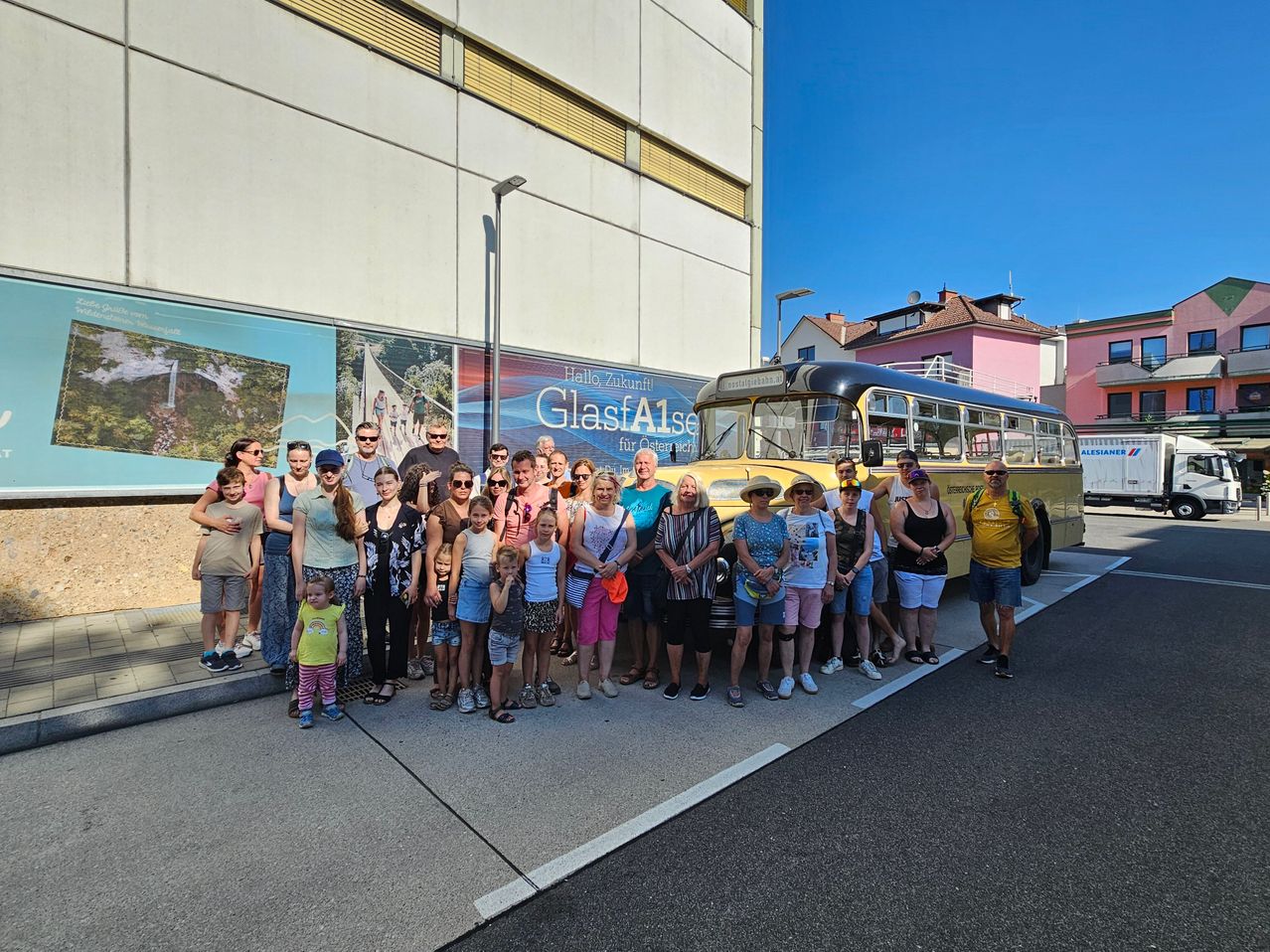 Eine Gruppe von Menschen steht vor einem gelben Bus mit einem Banner, auf dem 'GlasfAise' steht. Sie alle lächeln und scheinen auf einer Tour zu sein.