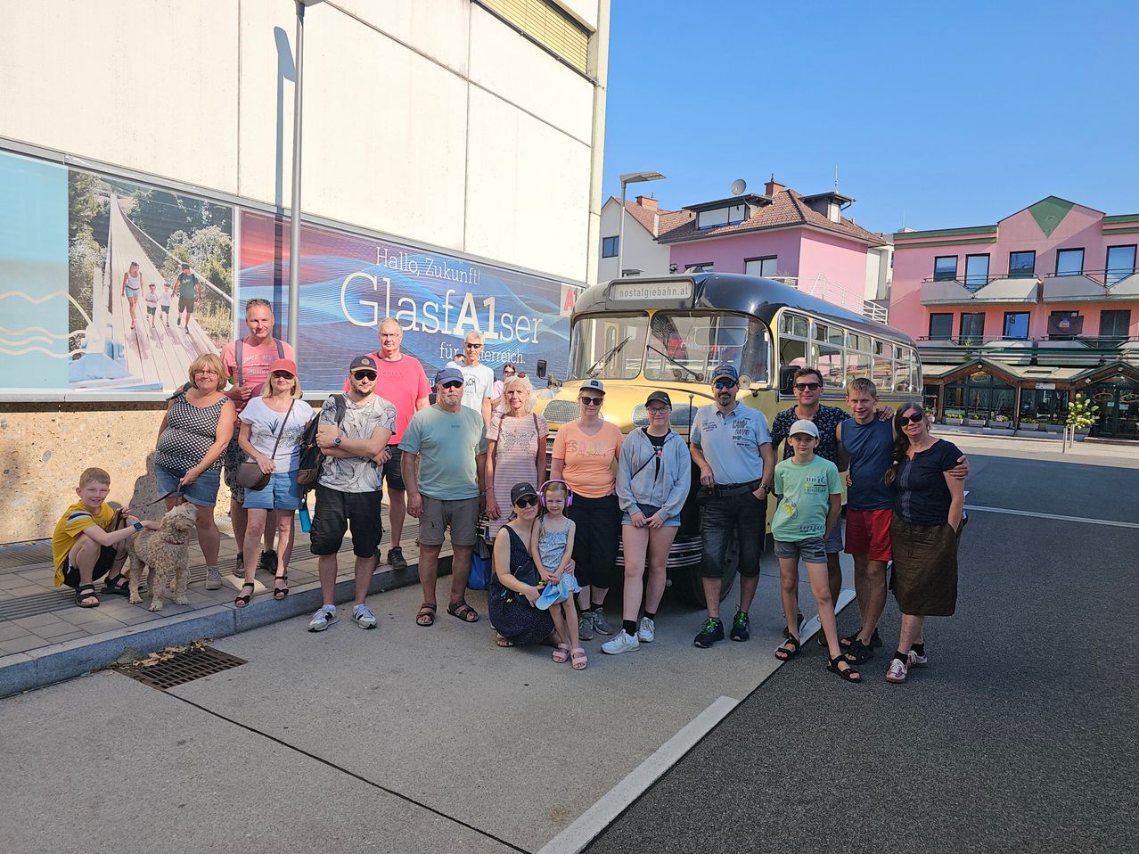 A group of people, including adults and children, are standing in front of a yellow bus with the text 'GlasA1ser' on the side. They are all smiling and posing for a photo.