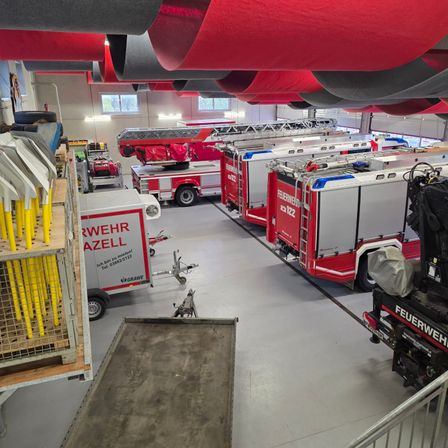 Eine Feuerwehrstation mit mehreren roten und weißen Feuerwehrfahrzeugen im Inneren, mit Werkzeugen und Ausrüstung an der Seite sichtbar.