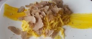 Ein weißer Teller enthält ein Gericht mit Pasta, gelber Sauce und mit gehobeltem Trüffel bestreut.