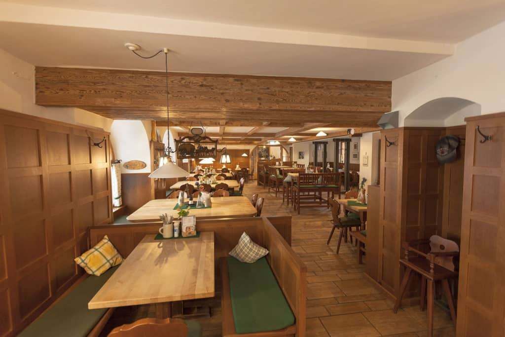 Ein gemütliches Restaurant mit Holztischen und -bänken, beleuchtet von warmen Lampen. Die Decke ist mit Holzbalken versehen und der Boden ist gefliest. Die Wände sind mit Holzpaneelen verziert.