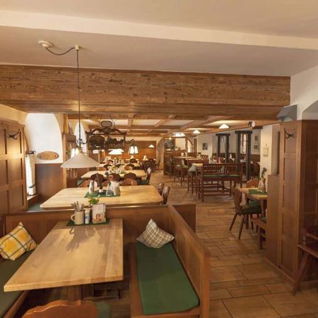 Ein gemütliches Restaurant mit Holztischen und -bänken, beleuchtet von warmen Lampen. Die Decke ist mit Holzbalken versehen und der Boden ist gefliest. Die Wände sind mit Holzpaneelen verziert.